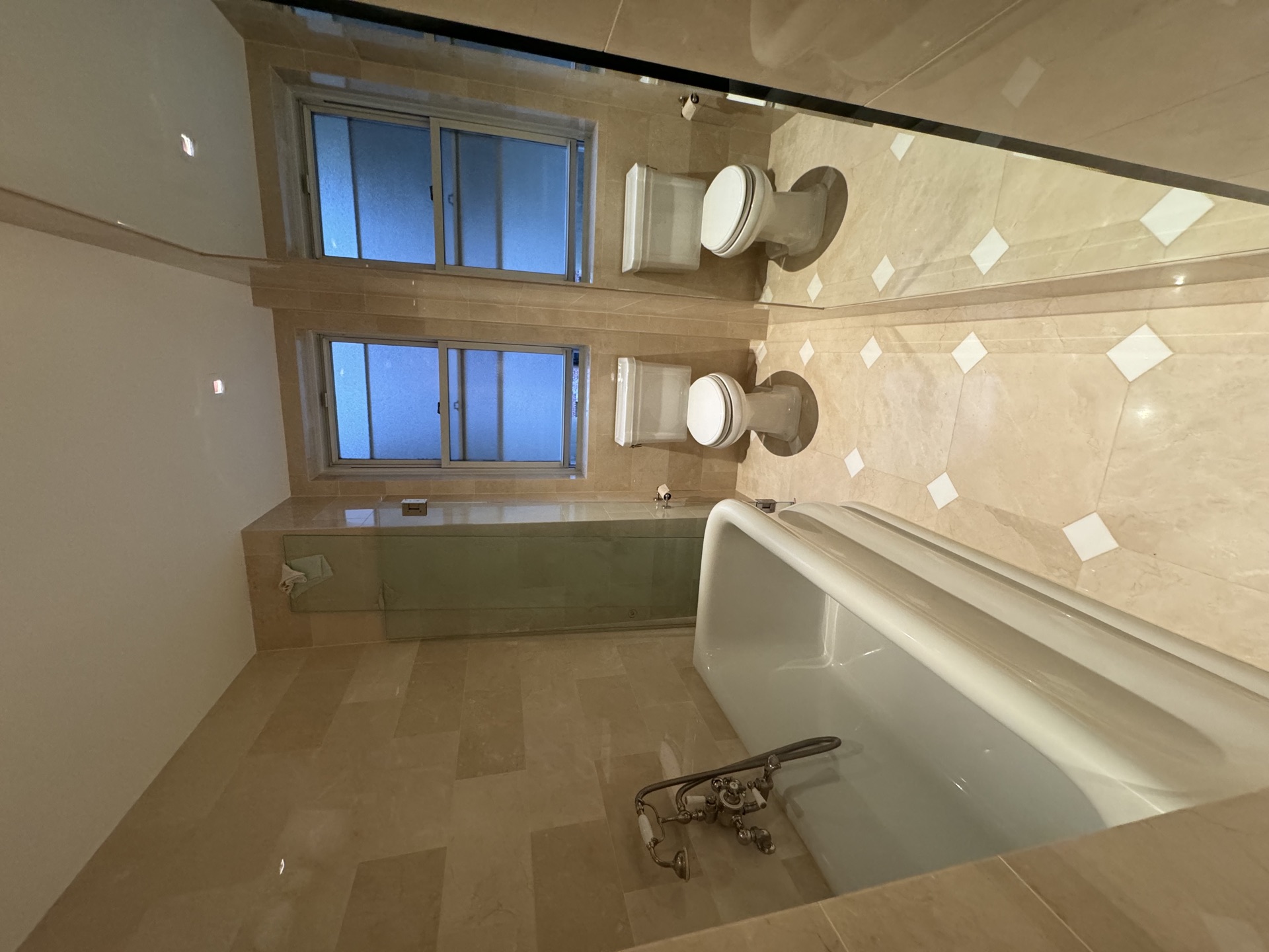 Marble-tiled bathroom with freestanding soaking tub, cross-handle filler, and frosted windows